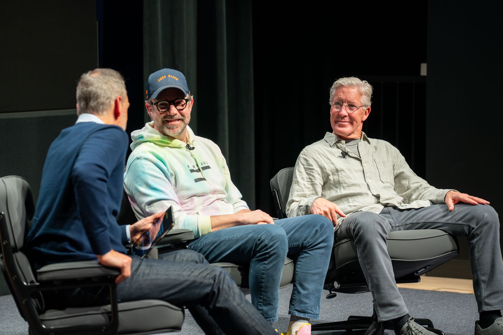 Ted Lasso clip playing on the big screen while Soni, Sudeikis, and Carroll watch from the stage